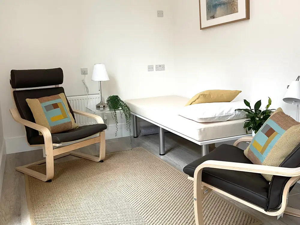 Therapy room with patient bed and leather chairs.