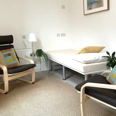 Therapy room with patient bed and leather chairs.